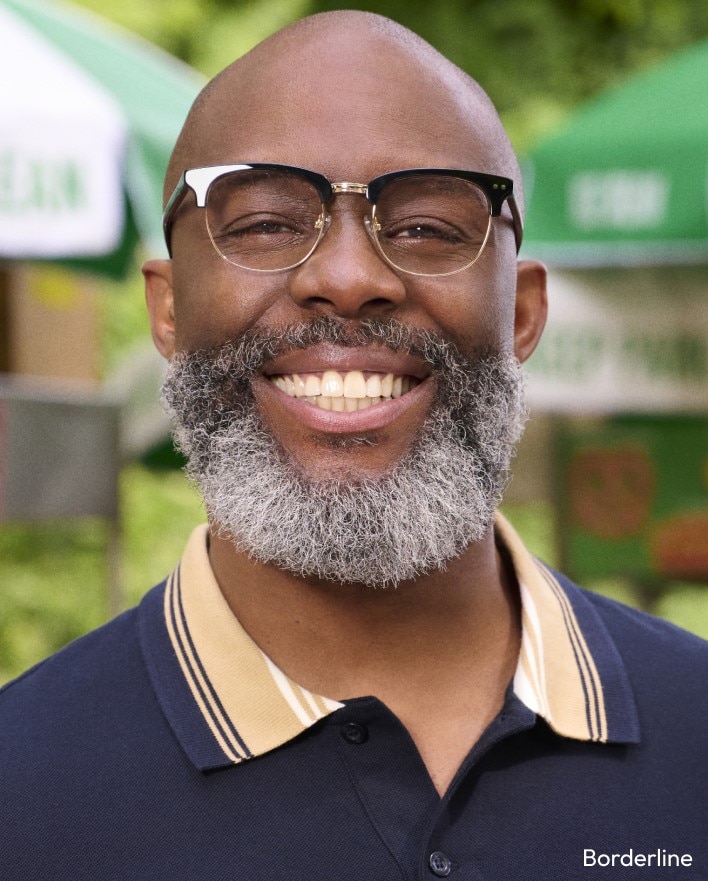 A man with a beard smiling and wearing browline-style eyeglasses