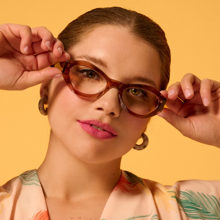 A woman in front of a yellow background wearing eyeglasses with thick brown frames 