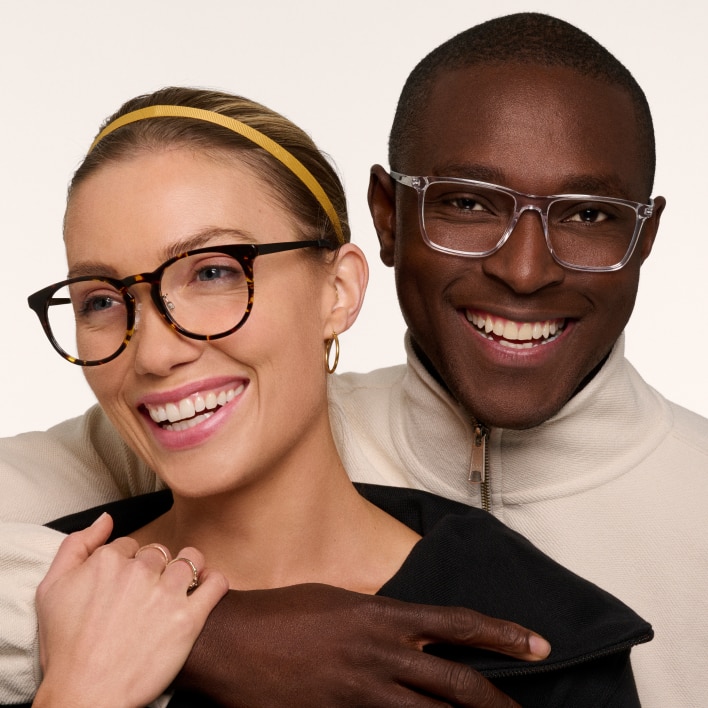 A man and woman facing the camera embracing and wearing eyeglasses