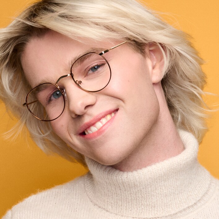 A person with mid-length blonde hair wearing round eyeglasses with metallic frames